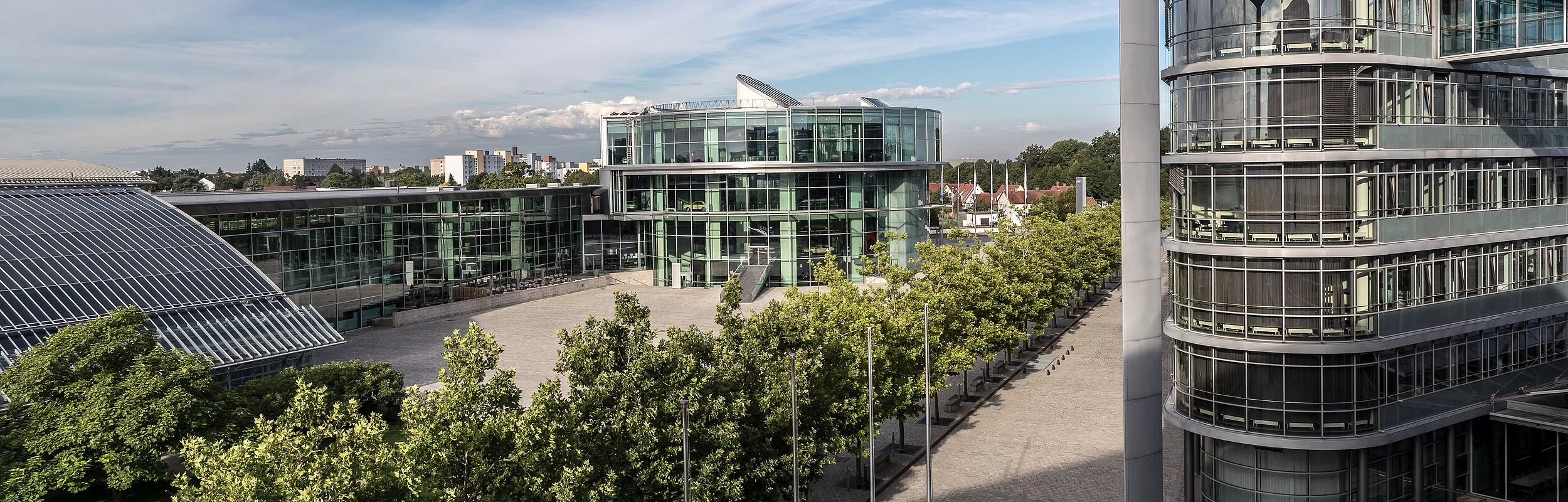 Das AUDI Forum von weitem und etwas erhöht liegt es idyllisch umgeben von Bäumen und Sträuchern. Davor erstreckt sich die Piazza, die AUDI Forum und Betriebsgelände miteinander verknüpfen.