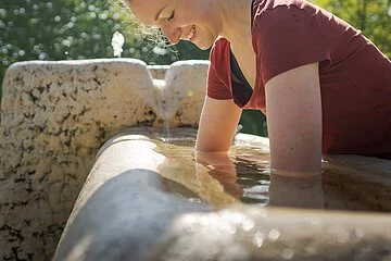Junge Frau hält Ihre Arme ins kalte Kneippwasser und hat sichtlich Spaß dabei.