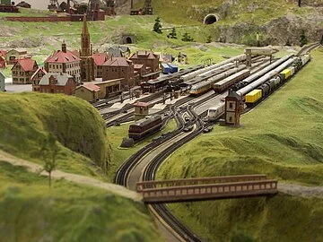 Miniaturland Treuchtlingen Eine Miniaturlandschaft umgeben von grün. Eisenbahnschienen und ein Dorf.