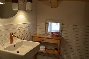 Eine Badezimmer der Gasthof Krone Kinding mit Waschbecken im Vordergrund und im Hintergrund ein Beistelltisch mit Spiegel