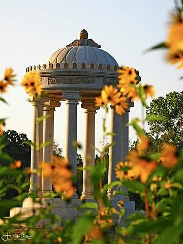 Fokus auf einen runden Steinpavillion im Schlosspark Dennenlohe. im Vordergrund gelbe Blumen.