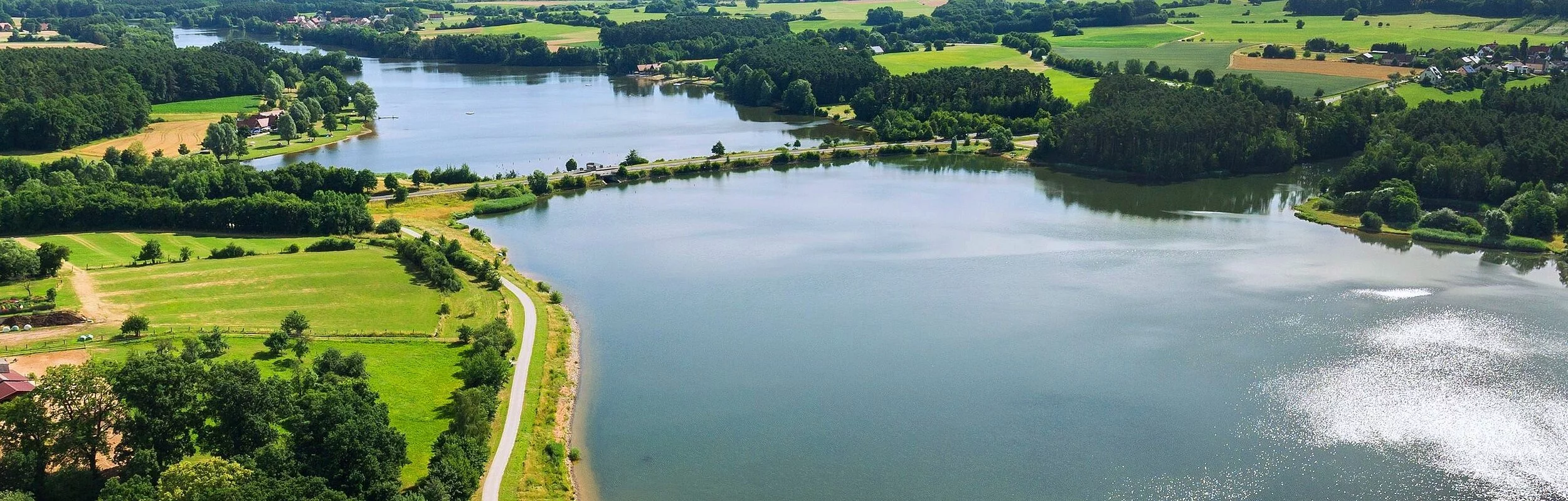 Luftbild von einem Teil des Rothsees. Der See ist umgeben von grünen Wiesen. Entlang des Ufers wachsen viele Bäume und Sträucher.