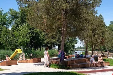 Blick auf Sitzgelegenheiten im Flussfreibad. Links im Hintergrund sieht man eine Rutsche.