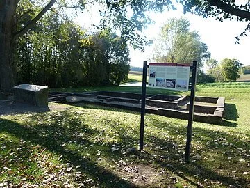 Römische Ruine Eine römische Ruine auf einer grünen Wiese. Davor steht eine Infotafel.