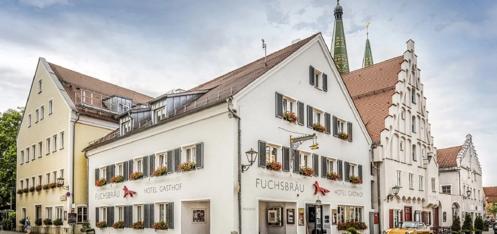 Das Hotel mit 3 Häusern an einer Straßenecke ist zu sehen. Im Hintergrund noch die beiden Türme der Stadtpfarrkirche.