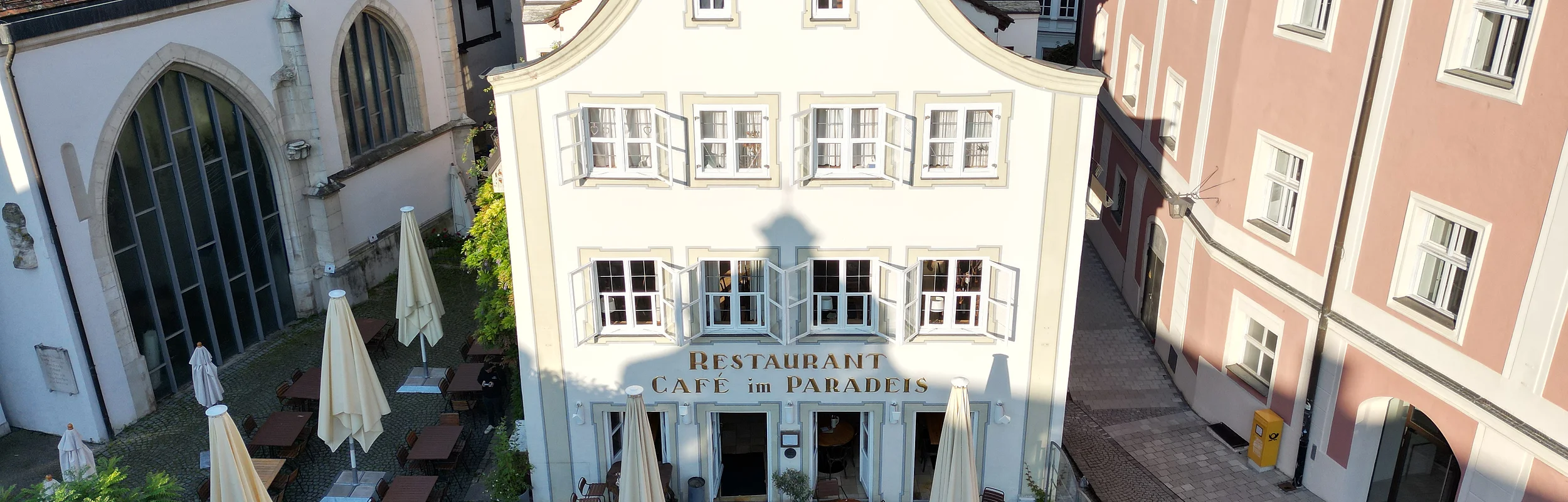 Das Gebäude des Café Paradeis in Eichstätt mit im Vordergrund der Terrasse mit Stühle, Tische und Sonnenschirme.