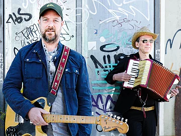 Stephan Zinner - Kabarett in Dietfurt Der Kabarettist steht zusammen mit seinem Musiker. Sie halten Gitarre und Akkordeon in der Hand.