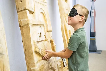 Ein Junge fühlt ein Kunstwerk mit seinen Händen und verschlossenen Augen.