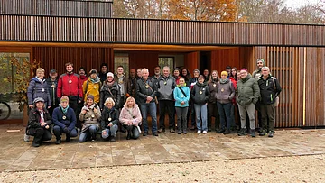 Runder Tisch Umweltbildung Etwa 30 Naturparkführer stehen vor dem Holzgebäude des Walderlebniszentrums in Schernfeld