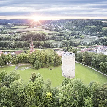 Heinrichsturm und Burgberg aus der Vogelperspektive. Im Hintergrund ist das Donautal mit Sonne am Horizont.