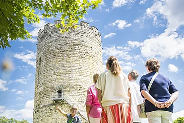 Vier Erwachsene nehmen an einer Marktführung vor dem Heinrichsturm teil. Der Himmel ist blau-weiß und oben spitzen grüne Äste in das Bild.