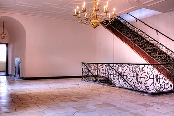 An den kahlen Wänden führt eine Treppe mit aufwändigen Details nach unten.