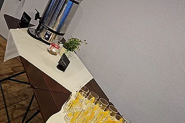 Auf dem Tisch ist ein Kaffeespender und einige Gläser mit Orangenscheiben platziert.