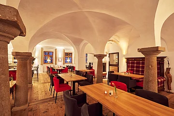 Speisesaal Post Berching Der Speisesaal mit Gewölbe und Bögen ist mit Holzischen und roten/schwarzen Stühlen ausgestattet.