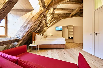 Doppelzimmer mit Dachschräge Post Berching Das Doppelbett befindet sich unter der Dachschräge im Zimmer, die rote Couch steht vorm Fenster.