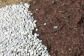 Weiße Kieselsteine grenzen an eine Fläche mit braunem Mulch.