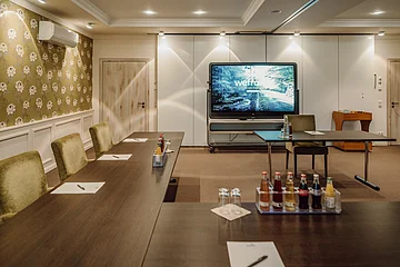 Tagungen Hotel Eisvogel Konferenzraum mit Tischen, Stühlen, Getränken und einem großen Bildschirm an der Wand.