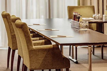 Tagungen Hotel Eisvogel Konferenztisch mit Stühlen, Schreibunterlagen und Stiften. Auf dem Tisch stehen Getränke und Gläser.