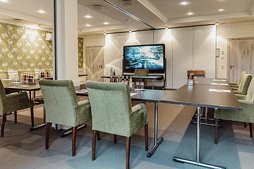 Tagungen Hotel Eisvogel Konferenzraum mit grünen Stühlen, Tischen, Getränken und einem großen Bildschirm an der Wand.