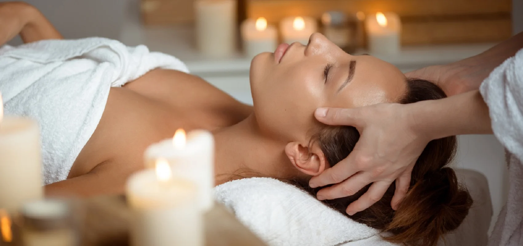 Person erhält Kopfmassage in einem Spa, umgeben von brennenden Kerzen.