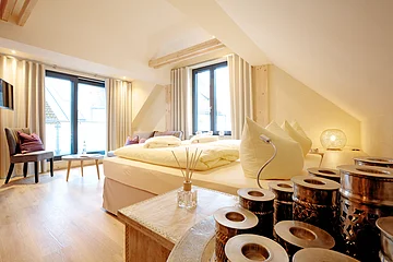 Idylle zu zweit Hotel Die Gams Helles Schlafzimmer mit Doppelbett, großen Fenstern, Holzboden und dekorativen Kissen. Ein Tisch mit Stühlen steht am Fenster.