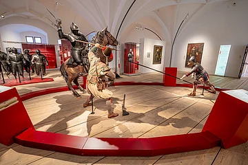 Ausstellung mit mittelalterlichen Rüstungen und Figuren in Kampfpose in einem Museum.