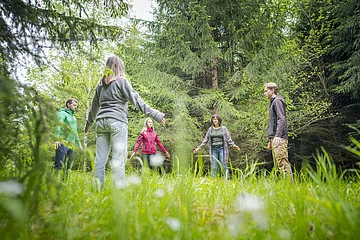 Fünf Personen stehen im Kreis auf einer Waldlichtung und halten die Arme leicht ausgestreckt.