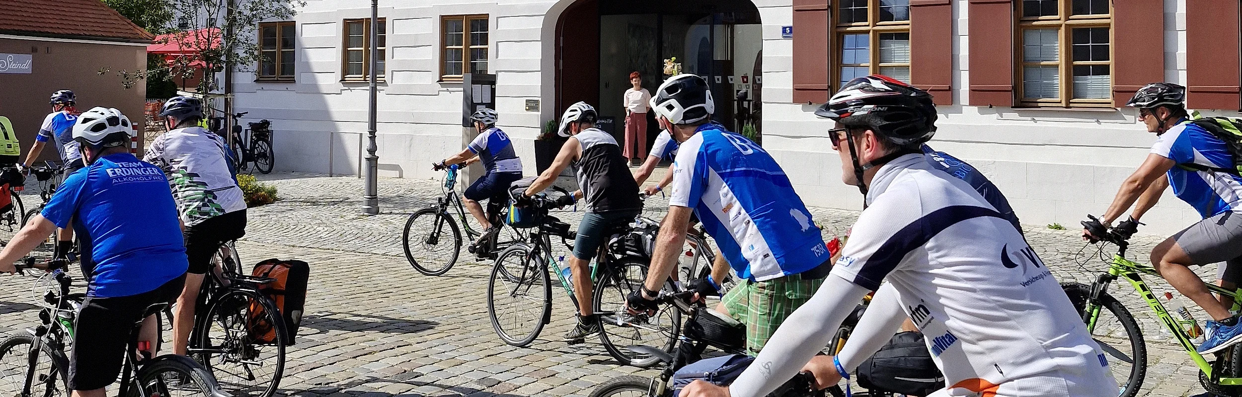Radfahrergruppe auf Kopfsteinpflaster vor einem historischen Gebäude mit rotem Dach.