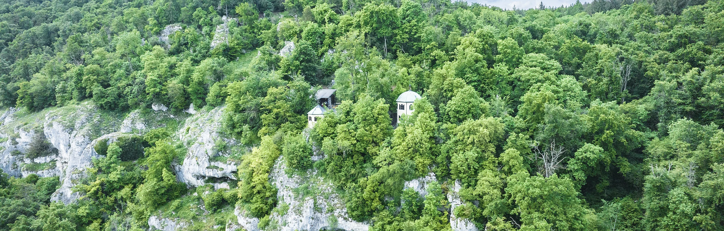Dichte bewaldete Hügel mit zwei kleinen Gebäuden auf einem Felsvorsprung.