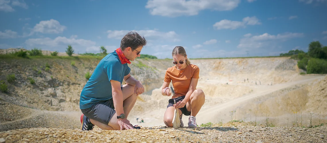 Zwei Personen knien auf einem steinigen Gelände und untersuchen den Boden.