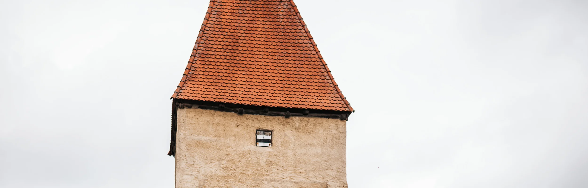 Zwei Radfahrer fahren an einem historischen Stadttor mit rotem Dach und Durchfahrt vorbei.
