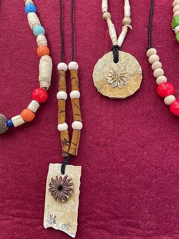 Naturschmuck Nahaufnahme von handgefertigten Halsketten mit Naturstein- und Holzperlen auf rotem Stoff.