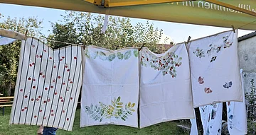 Vier weiße Tücher mit Pflanzenmustern hängen an einer Wäscheleine im Garten.