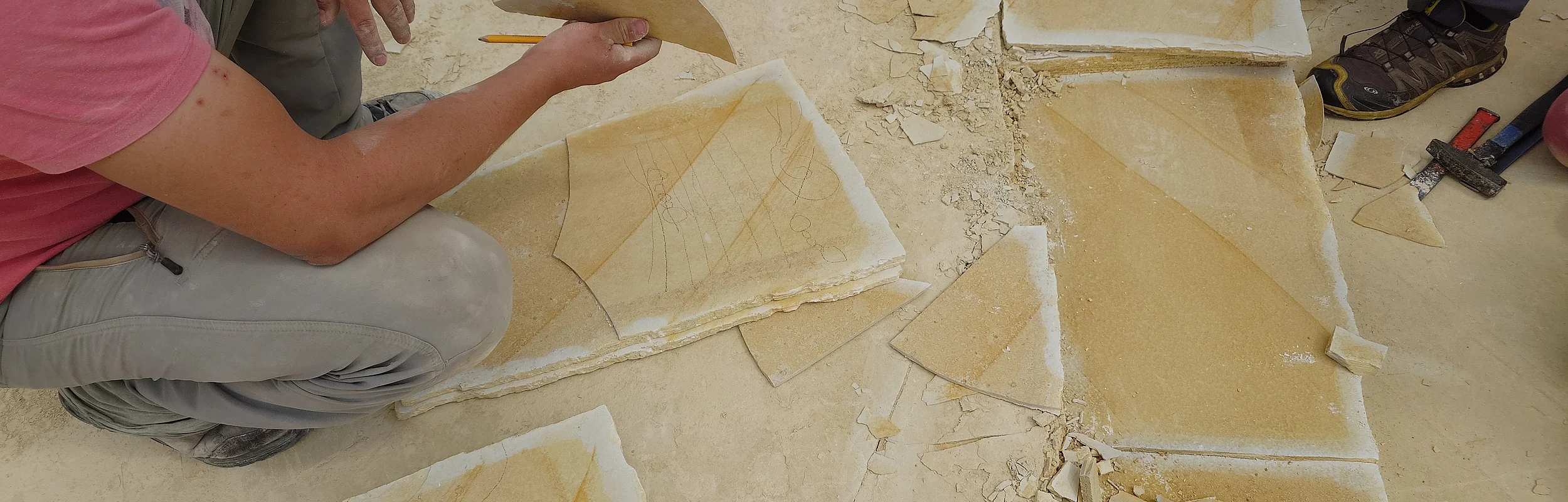 Mehrere Personen bearbeiten und zerbrechen große, flache Steinplatten im Steinbruch.