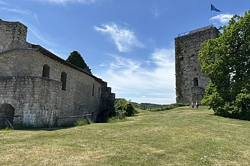 Im Zentrum des Bildes ist ein Innenhof zu sehen. Rechts vor einem blauen Himmel sieht man den Turm einer Burg. Links sieht man ein weiters Burggebäude.