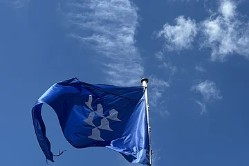 Vor einem blauen Himmel mit wenigen Wolken ist die blaue Flagge der Burg Pappenheim zu sehen.