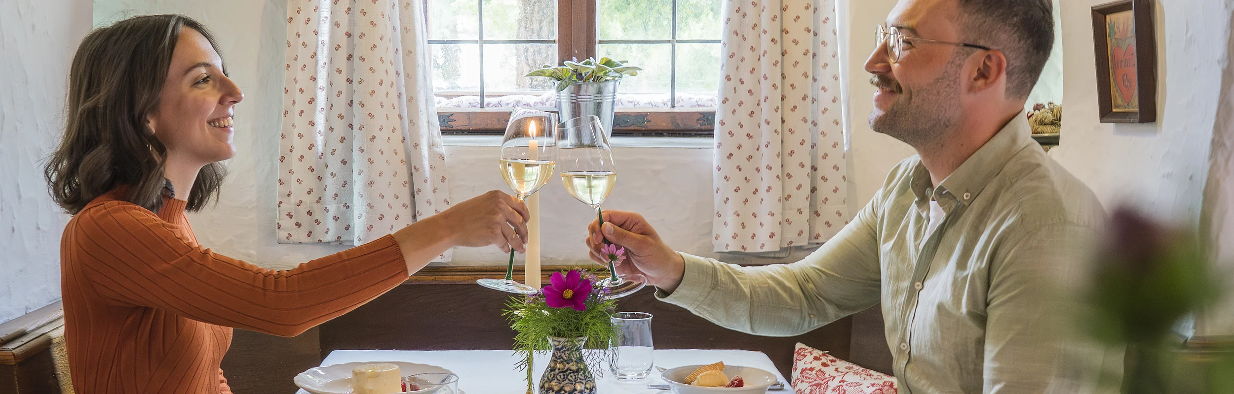 Ein Pärchen sitzt am gedeckten Tisch in der gemütlichen Gaststube des Restaurants "Zum Klosterbräu" in Bergen im Naturpark Altmühltal. Die beiden stoßen mit Weißwein an.