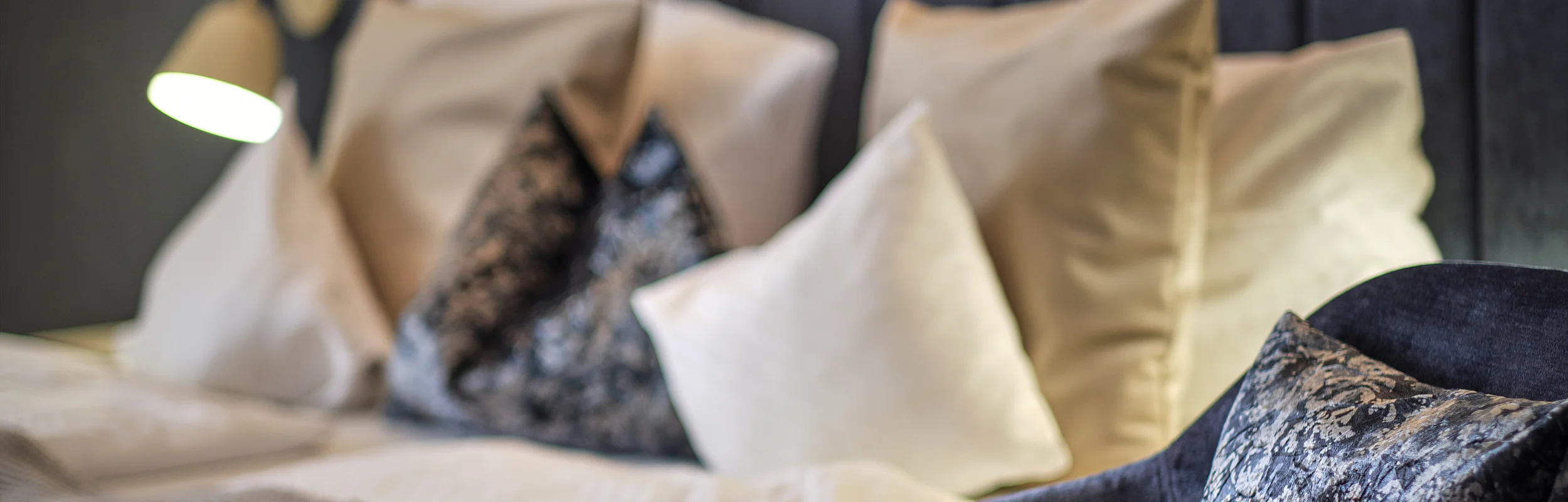 Bett mit mehreren Kissen und eine dunkelblaue Sitzgelegenheit mit gemustertem Kissen im Vordergrund.