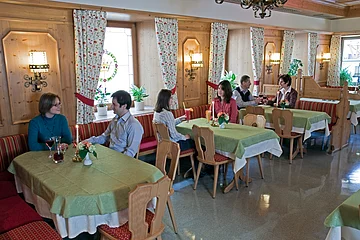 Gastraum mit Holzwänden, grünen Tischdecken, mehreren Gästen an Tischen und Kerzenlicht in einem Restaurant.