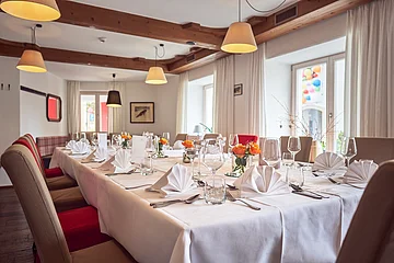 Großer Esstisch mit weißer Tischdecke, gefalteten Servietten, Gläsern und Blumen in einem Raum mit Holzdecke.