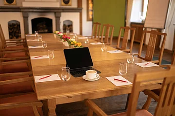 Konferenztisch mit Stühlen, Tablet, Kaffeetasse, Gläsern, Notizblöcken und Stiften in einem Raum mit Kamin.