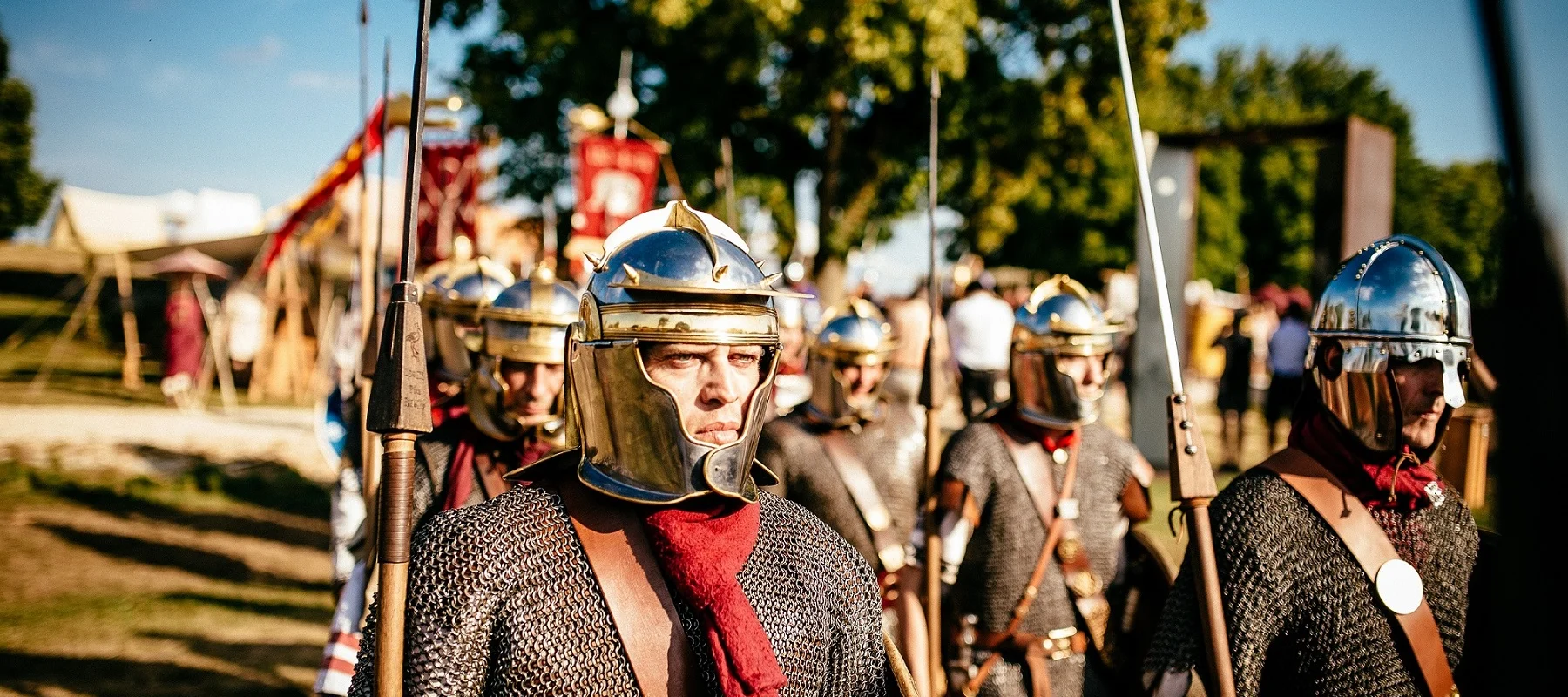Gruppe von Menschen in römischer Rüstung mit Helmen und Speeren bei einem historischen Nachstellen im Freien.