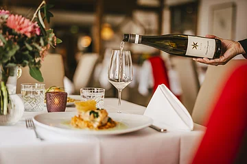 Wein wird aus einer Flasche in ein Weinglas auf einem gedeckten Tisch in einem Restaurant eingeschenkt.