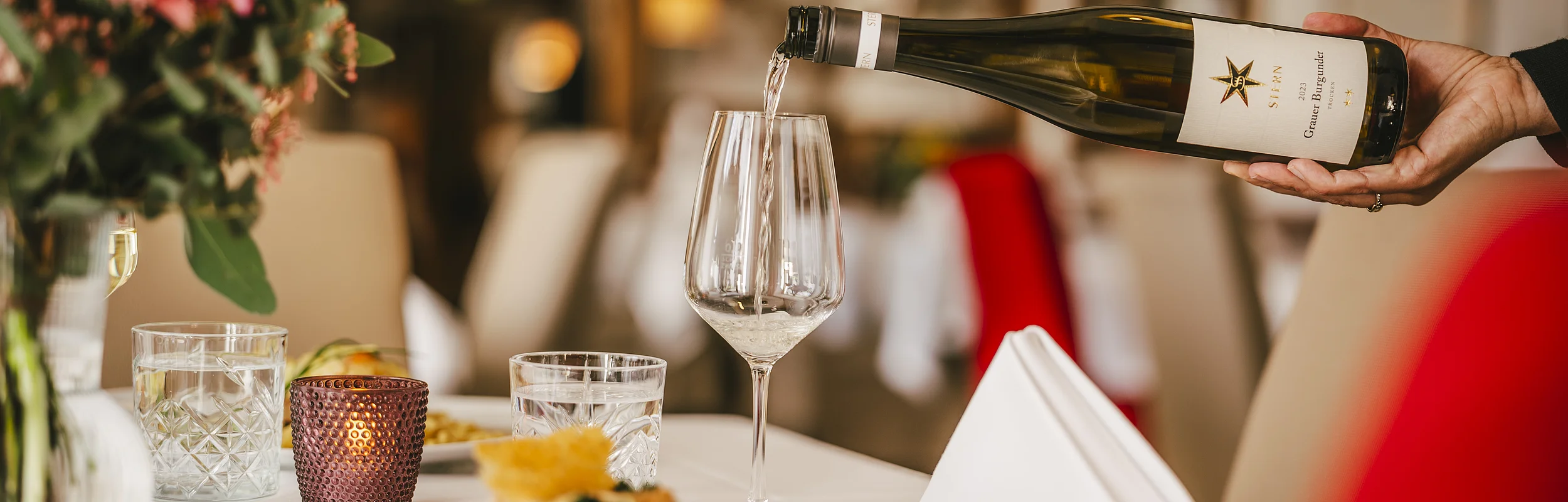 Wein wird aus einer Flasche in ein Weinglas auf einem gedeckten Tisch in einem Restaurant eingeschenkt.