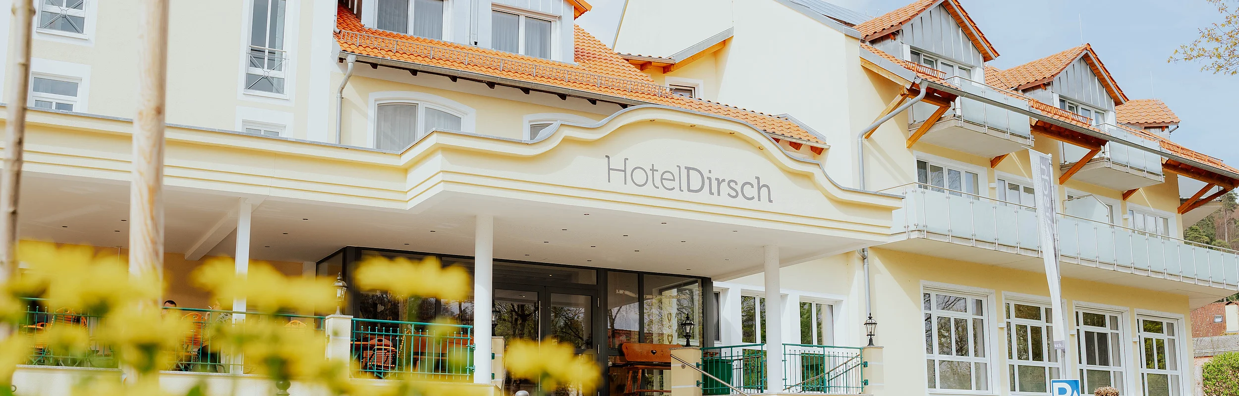 Eingangsbereich des Hotels Dirsch mit Treppe, Geländer und gelben Blumen im Vordergrund.