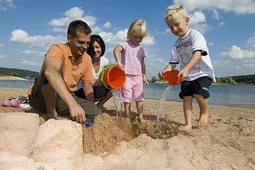 Eine vierköpfige Familie spielt am Strand des Brombachsees in Ramsberg. Die zwei Kinder erfreuen sich am sandeln und genießen die Zeit.