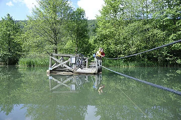 Mit eigener Kraft ziehen Radfahrer auf dem Holzfloß über den Alten Kanal bei Dietfurt.